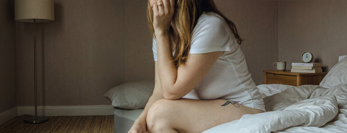 Female sitting on the side of bed, has her head in hands