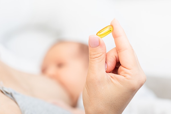 Mother holding yellow pill while breastfeeding newborn baby. Breastfeeding and medication concept