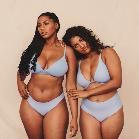 Self-confident young women wearing blue underwear in a studio. Two young women embracing their natural bodies and curves. Body positive young women standing together against a studio background.