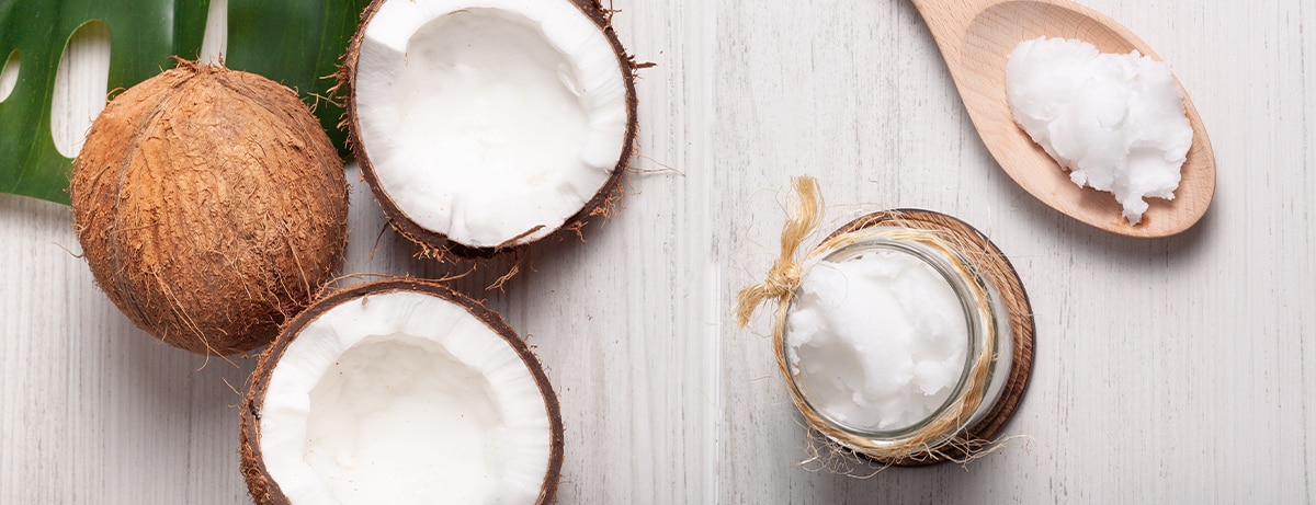 Still life of two coconuts, one of them cut in half, with a jar of coconut oil and a wooden spoon