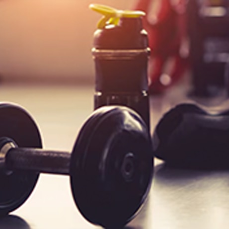 backlit shot of protein shaker and dumbell at the gym
