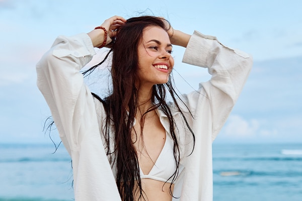 Brunette woman with long hair in a white shirt and shorts smile and happiness walking on the beach and having fun smile with teeth pulling hands into the camera selfies ocean, vacation summer travel