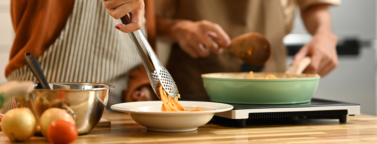 Young couple cooking spaghetti in a cozy kitchen. People, food and domestic life concept