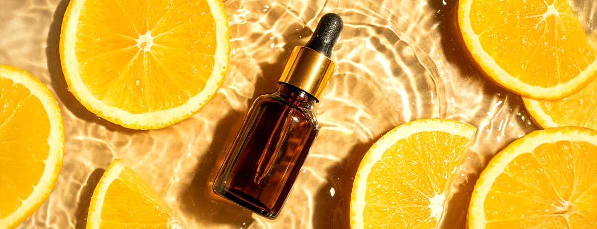 Dropper bottle with face brightening serum or essential oil and orange citrus slices in splashing water background, top view. Moisturizing organic vitamin C beauty, anti aging skin care concept.