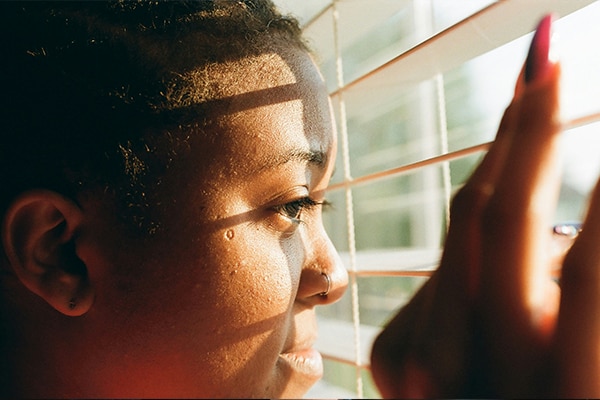 Female looking out of blinds at the sunshine