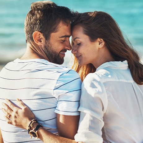 Hug, couple and relax on beach for love, commitment and bonding on summer vacation for honeymoon. Man, woman and back view together by ocean for romantic holiday, affection and weekend with embrace.