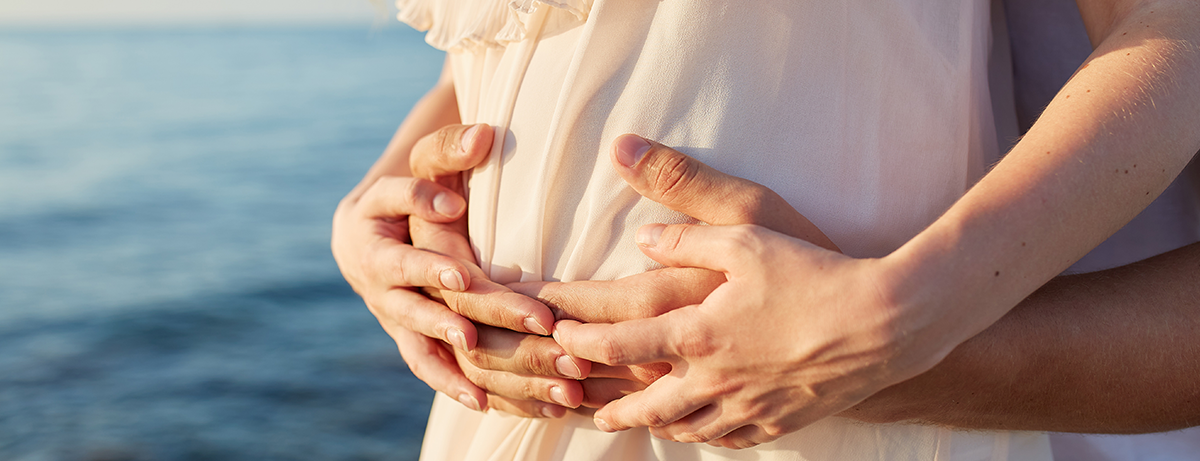 Close-Up Of The Hands Of A Man And A Woman On The Stomach Of Early Pregnancy on the background of a beautiful sea.