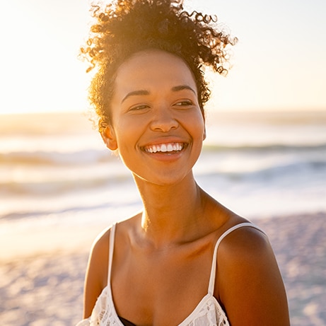Smiling young black woman in beachwear enjoy sunset at beach. Satisfied beautiful girl with afro hair relaxing at beach during sunrise with copy space. African american woman daydreaming.