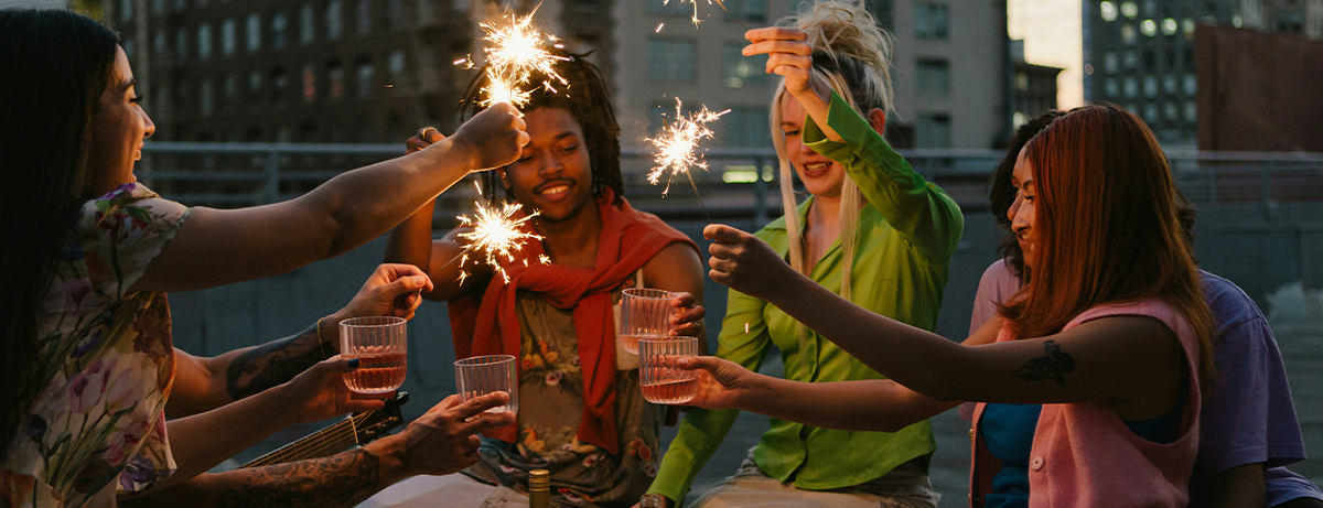 Friends sitting on rooftop with fireworks and glasses of drink
