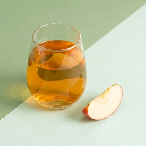 Glass of apple cider vinegar on green background