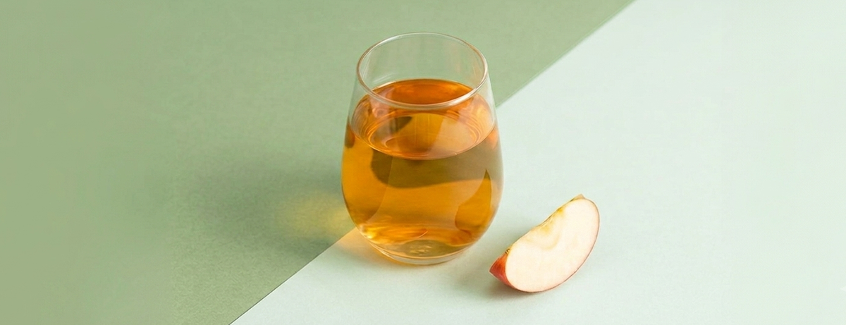 Glass of apple cider vinegar with apple slice on green background