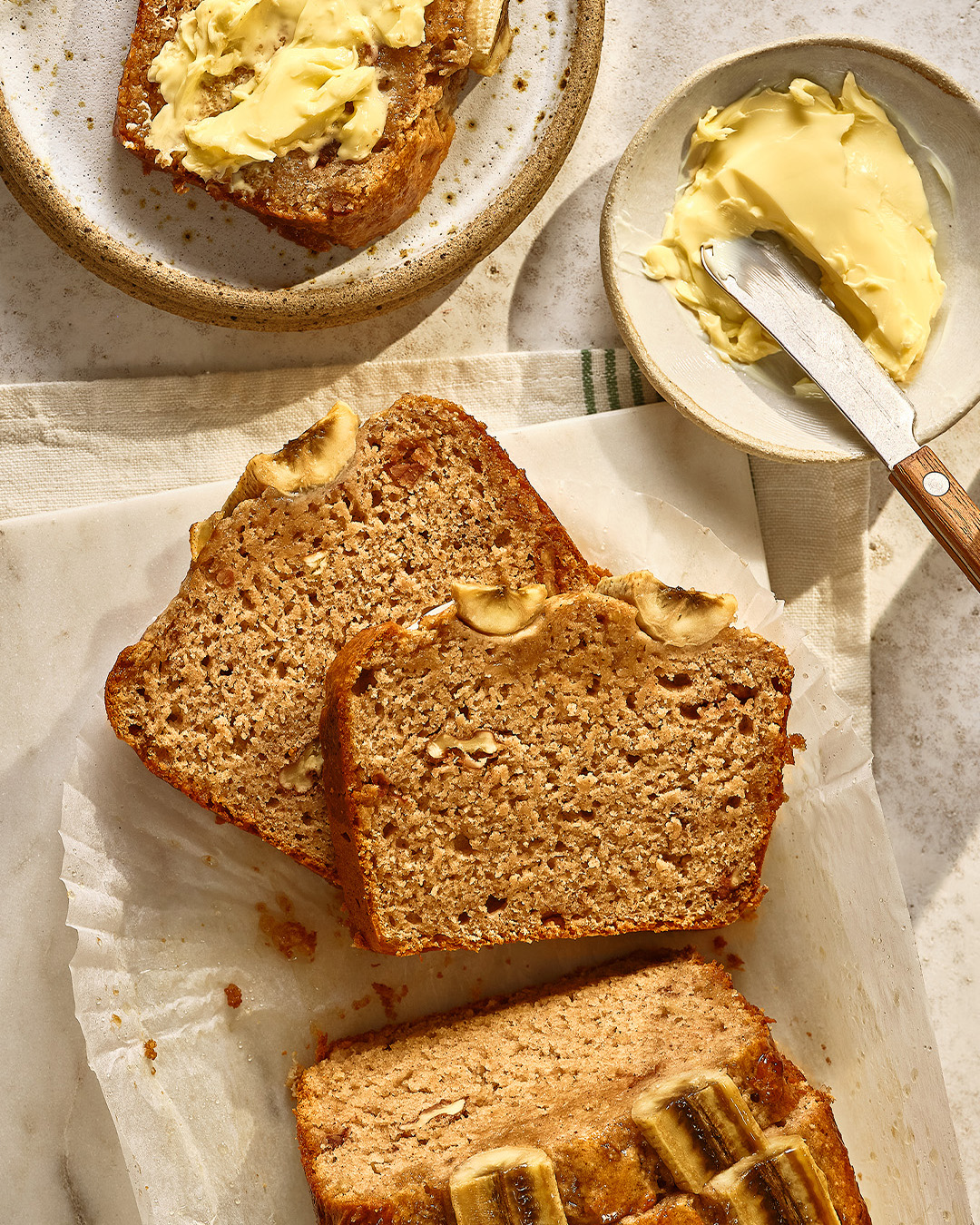 Banana bread on baking paper cut into slices with butter