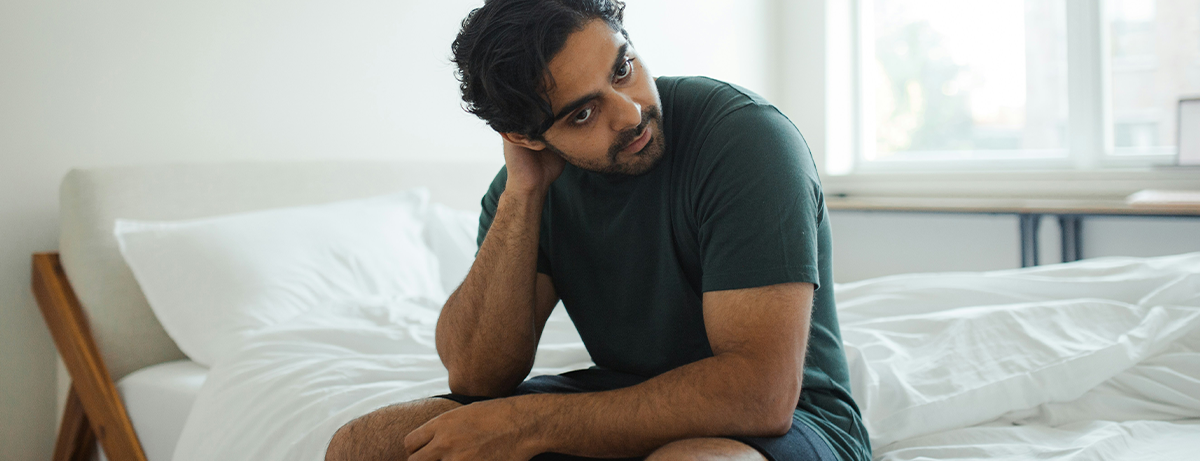 Male sitting on the side of a bed with a calm expression
