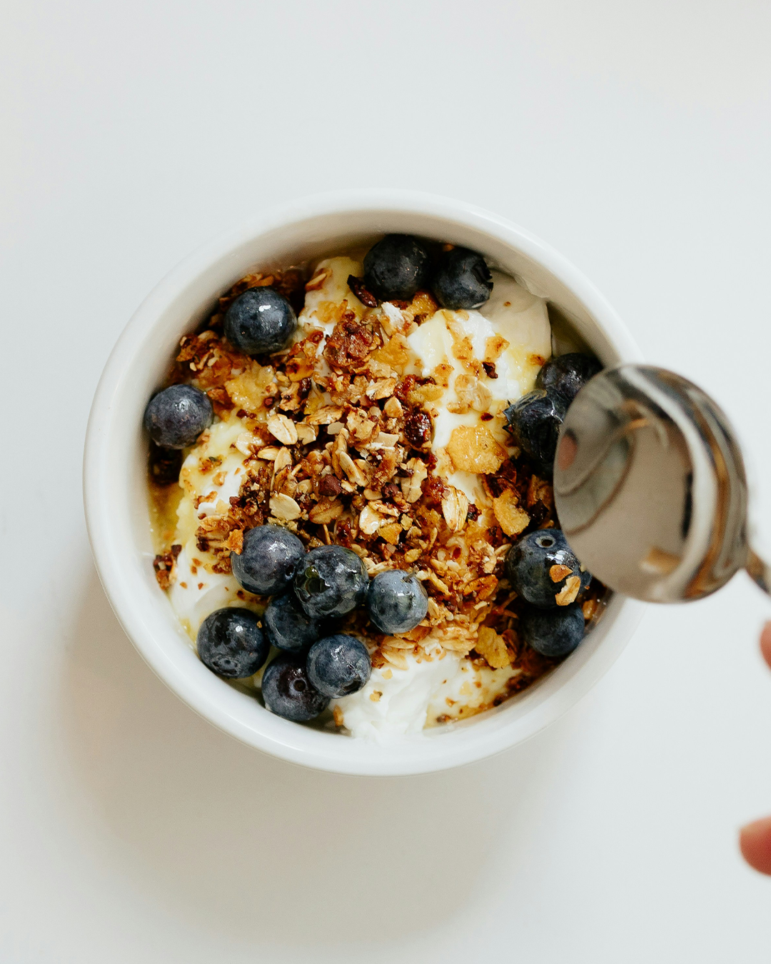 Hand dipping a spoon into a granola yoghurt bowl