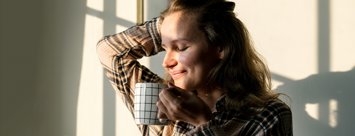 Female standing in living room with sunlight on face. Happy expression