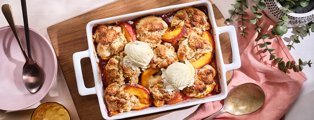 Gluten free peach cobbler in a white oven dish on a pink blanket