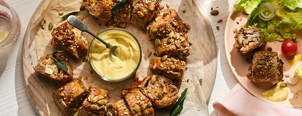 A gluten free sausage roll with a dip on a chopping board