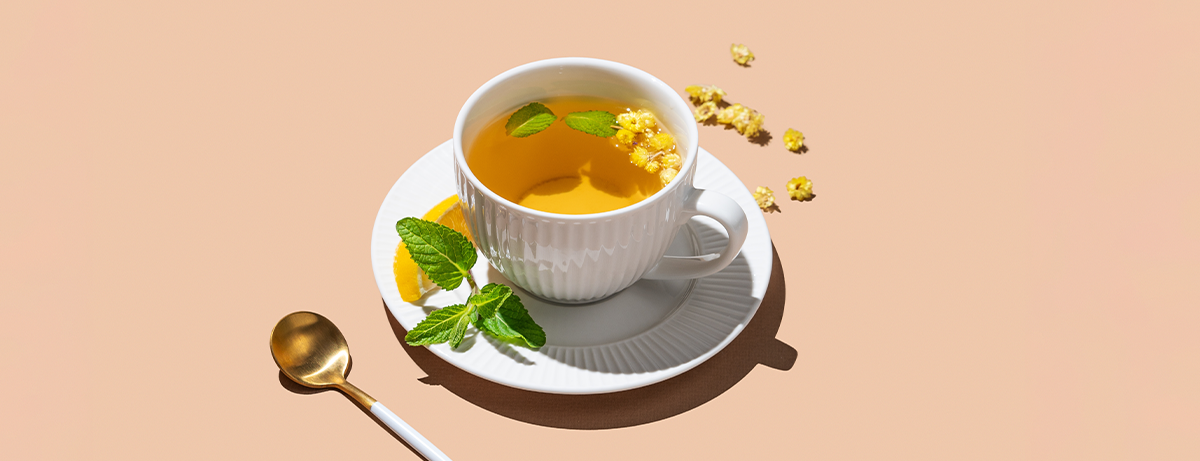 Cup of herbal tea with lemon and mint on beige background with spoon and morning shadows.
