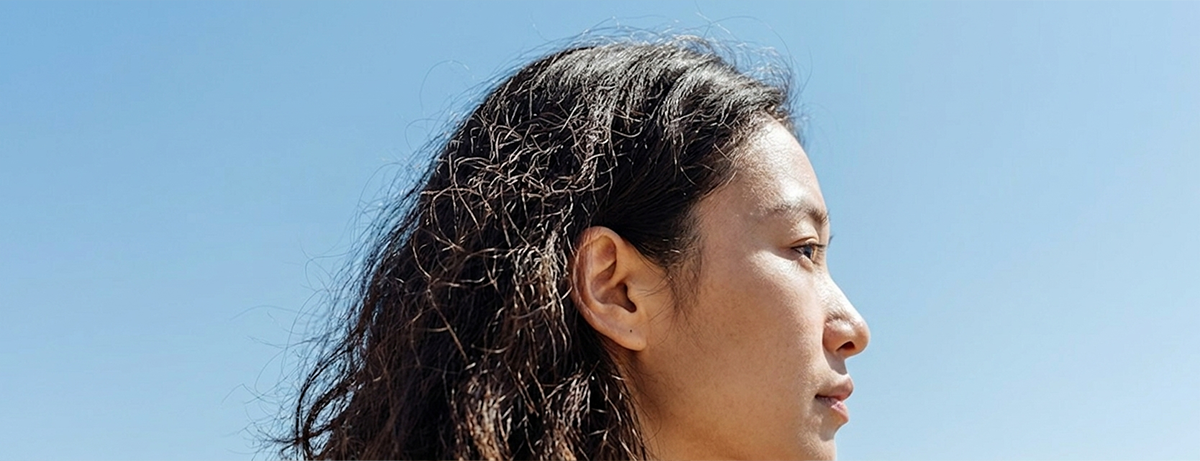 Close up of asian female with frizzy hair, blue sky background