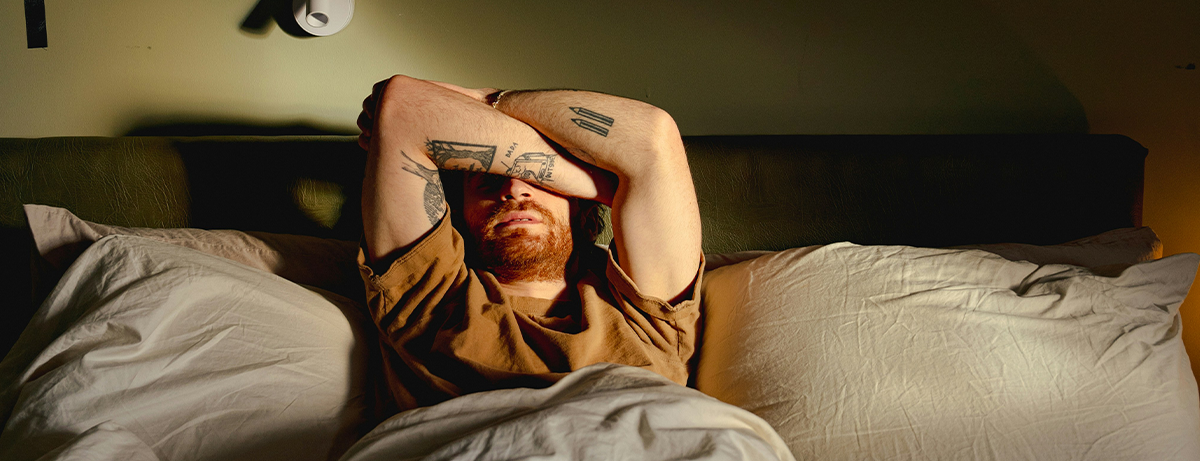 Male sat in bed with arms crossed over face