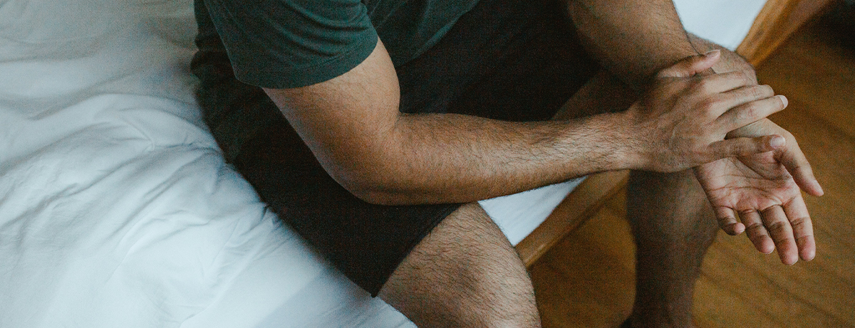 Male sitting on the edge of bed with hands together