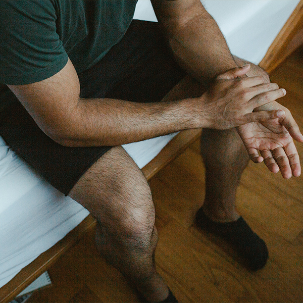 Male sitting on the edge of bed with hands together