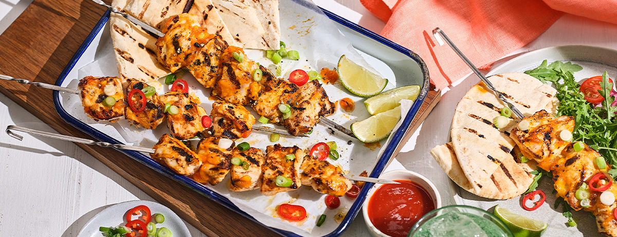 Portion of mango chicken skewers on a white oven dish with pitta