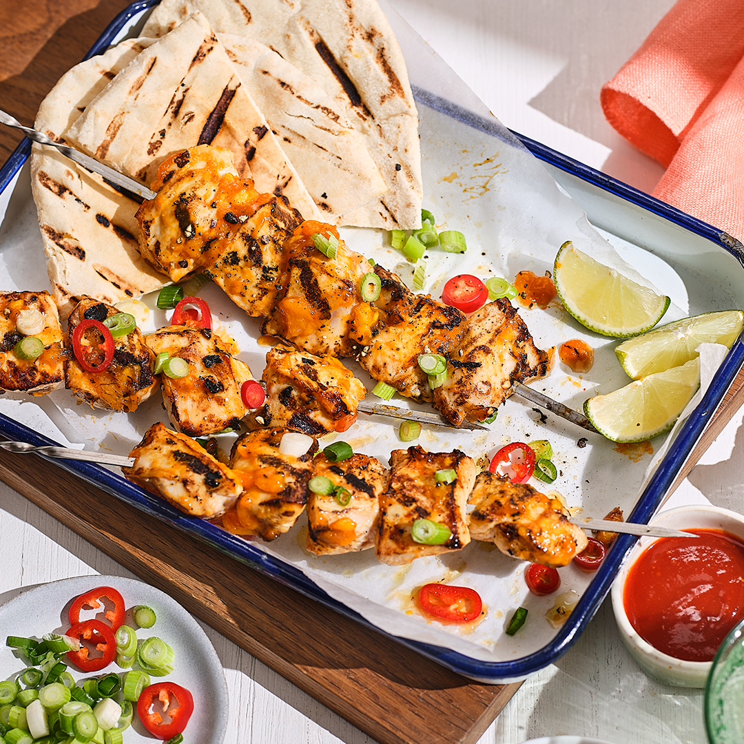 Portion of mango chicken skewers on a white oven dish with pitta