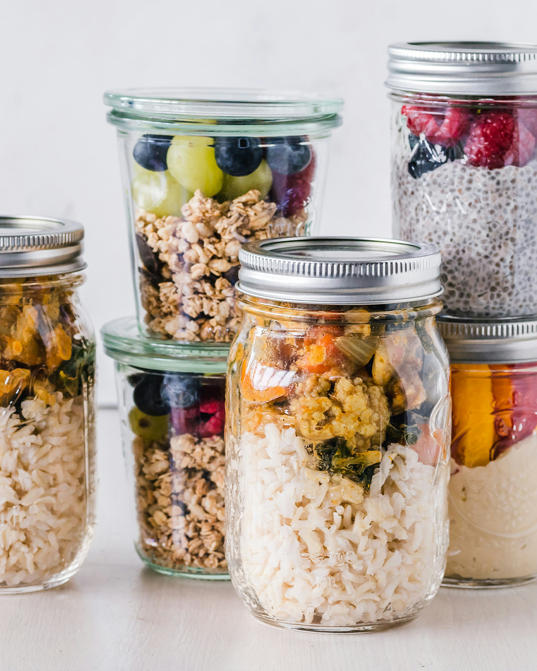 Glass jars of food meal prepped on a white background
