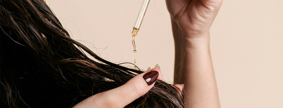 Close up of oil serum being put on brown hair