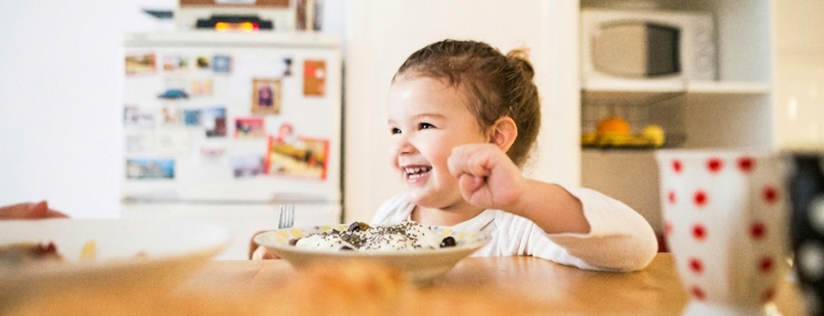 Girl sitting at the table, smiling. Eating yoghurt and omega-3 chia seeds