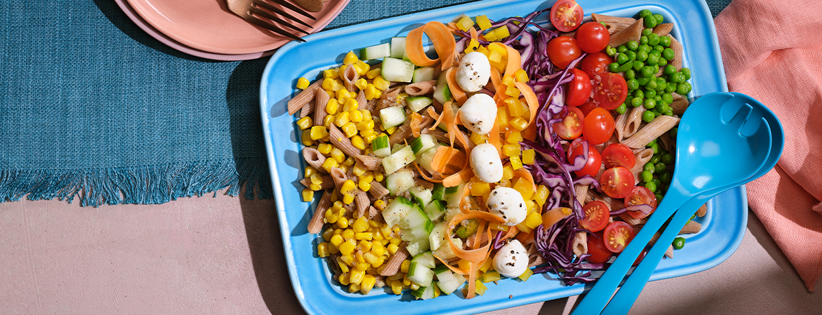 Rainbow picnic salad in plastic tub on blue blanket