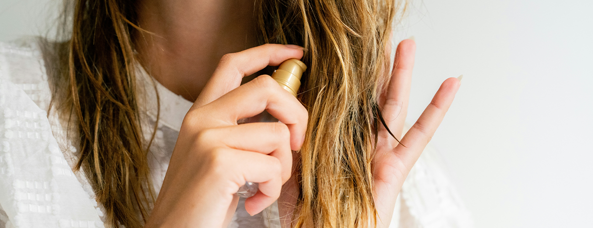 Female holding hair oil and spraying to long hair. Close up