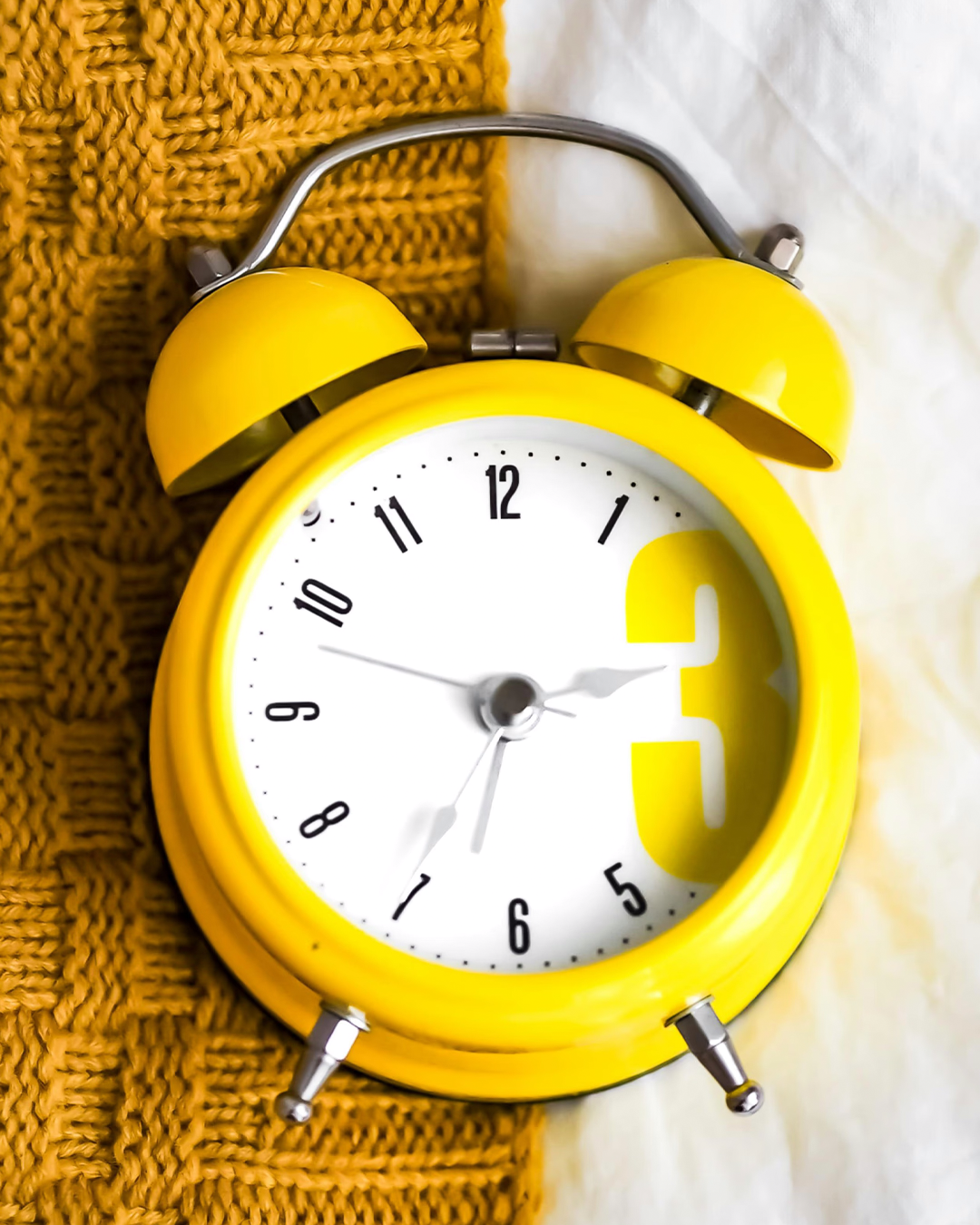 Alarm clock on yellow and white bedding