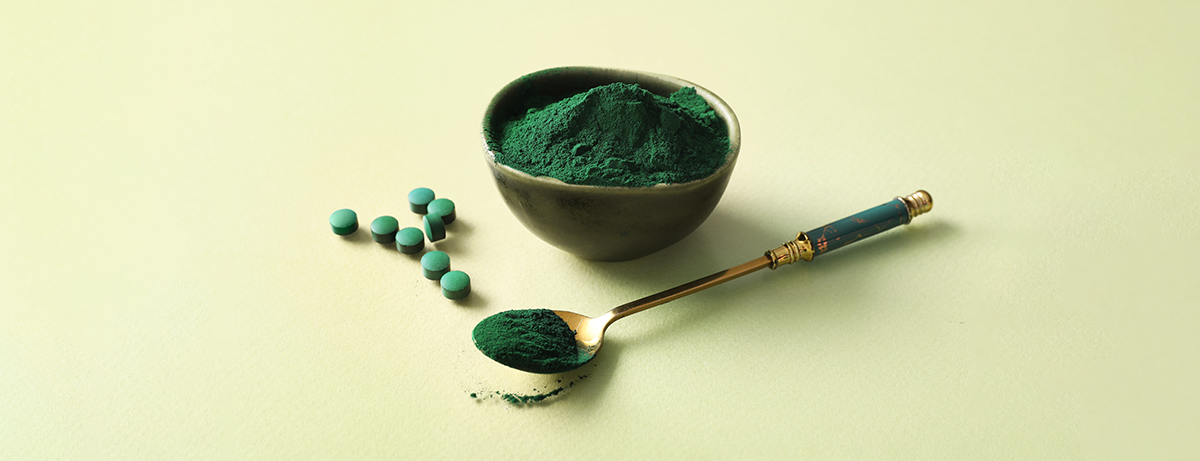 Bowl of spirulina and green supplements on green background