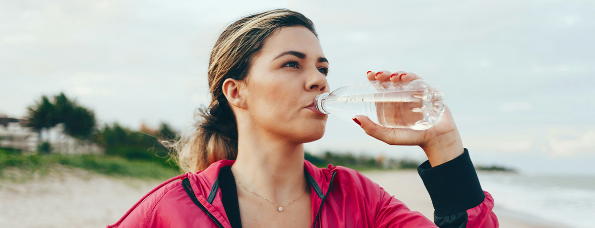 Female in sports clothing drinking water on the beach