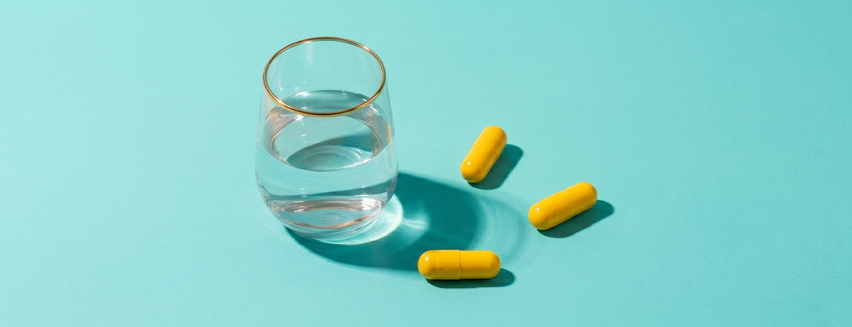 Glucosamine tablets and glass of water on blue background