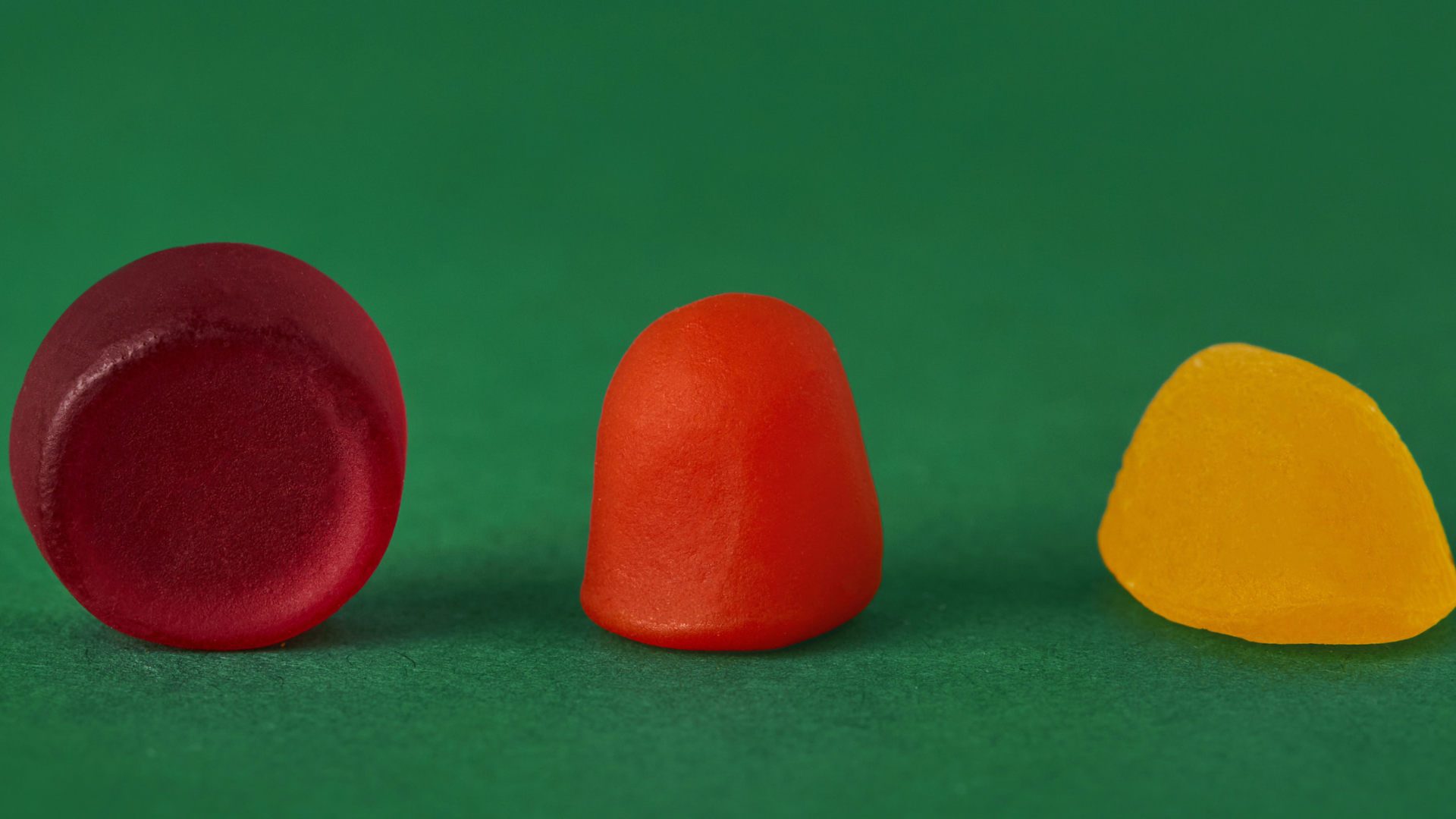 Red, orange and yellow gummies of different shape and size on green background