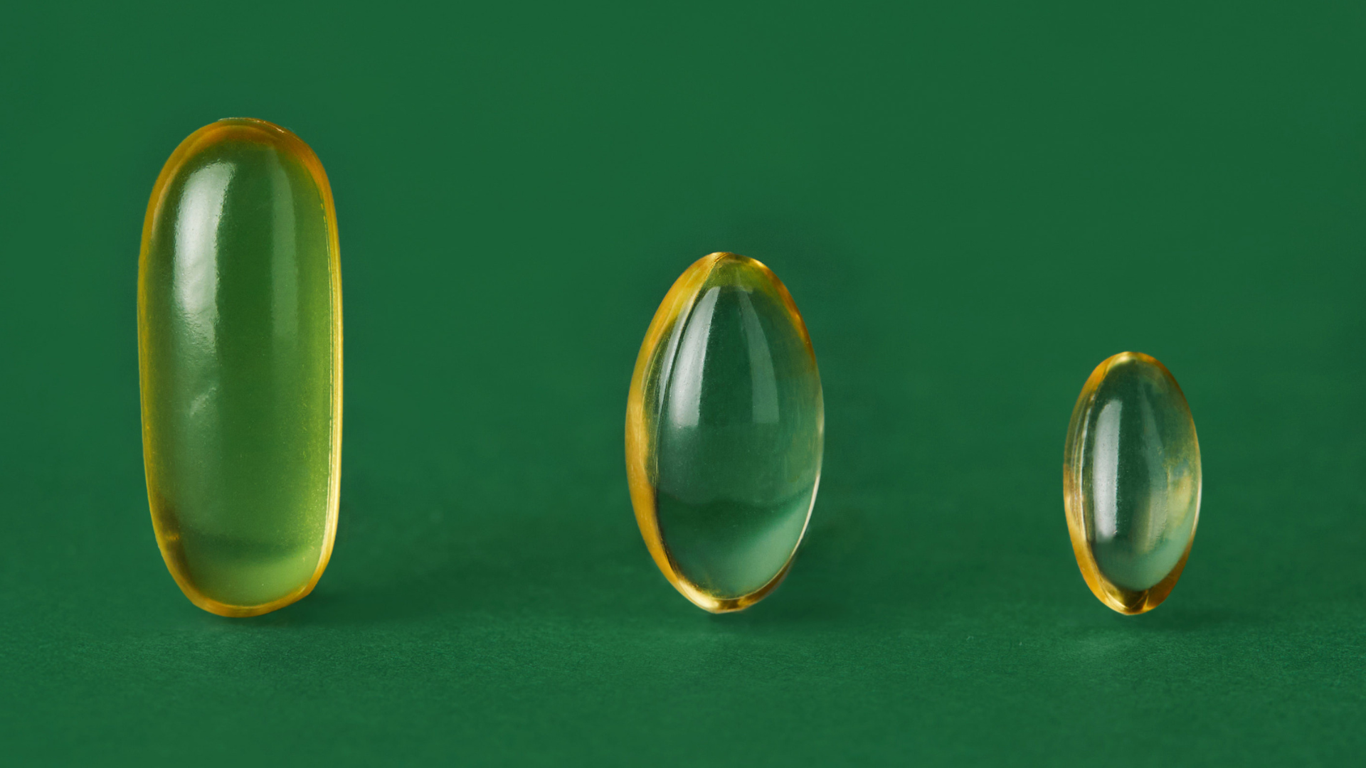 Three yellow translucent softgels of different shape and size on green background