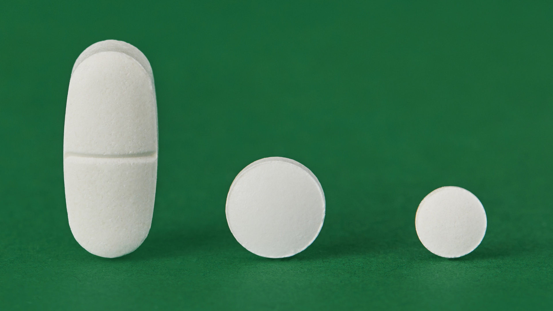 Three white tablets of different shape and size on green background