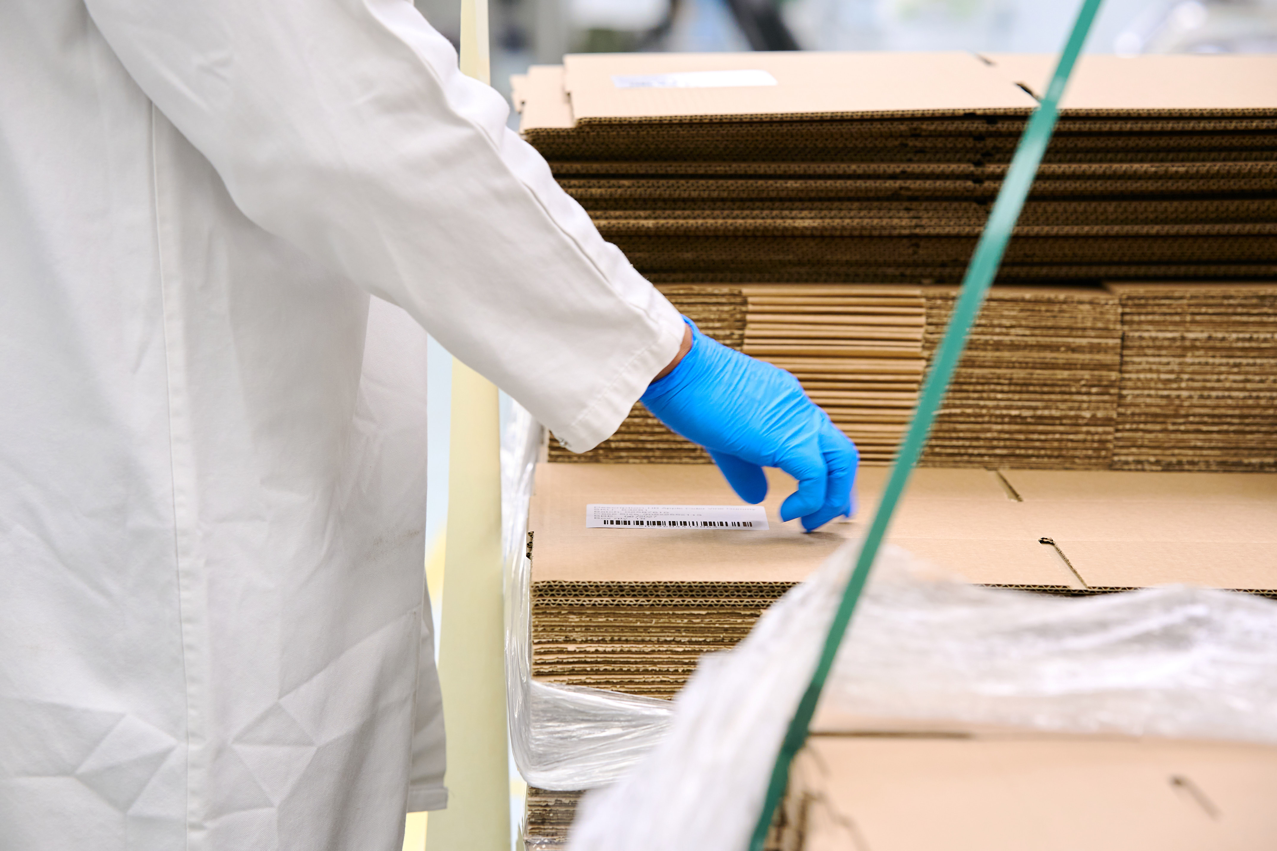 Production Operator in white gown and blue gloves checking a stack of new cardboard boxes