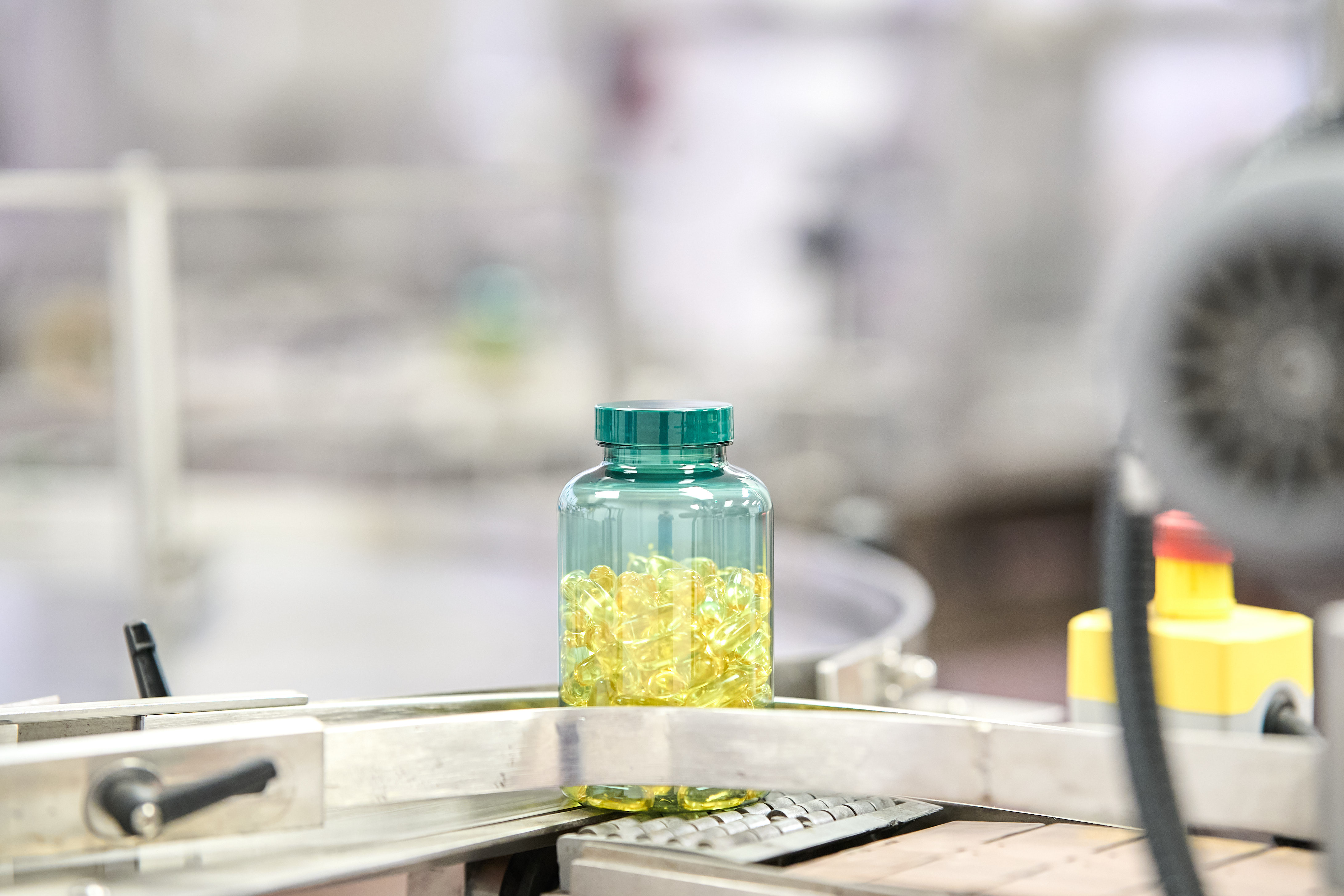 Translucent green bottle filled with translucent amber softgels on the production line without label
