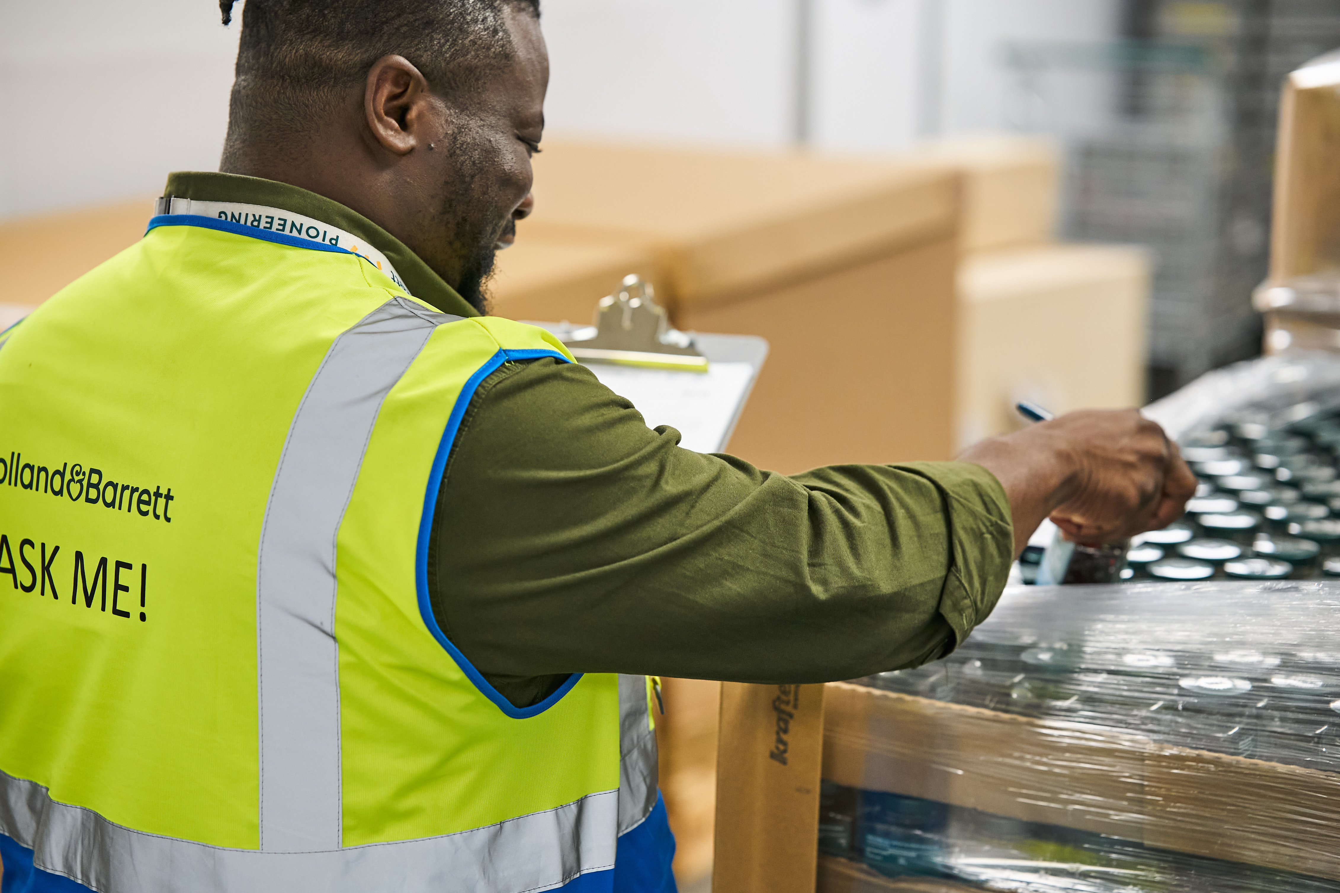 Quality Operator checking a finished product packed in a pallet, wearing a yellow hi-vis with ask me written on the back