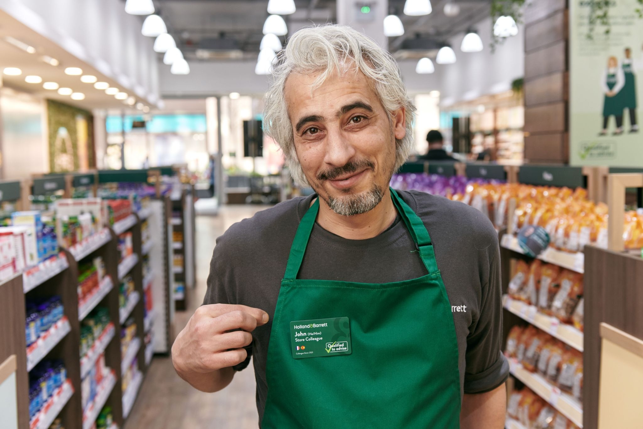 H&B store colleague showing their name tag and smiling in front of camera in store