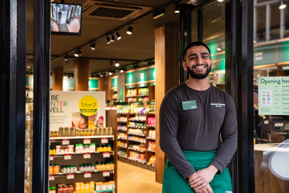 Colleague smiling and standing in front door of a H&B store